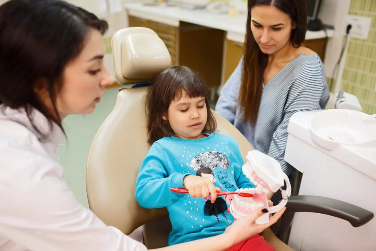 Pediatric dentist showing a child a tooth model to ease anxiety before a sedation dentistry visit
