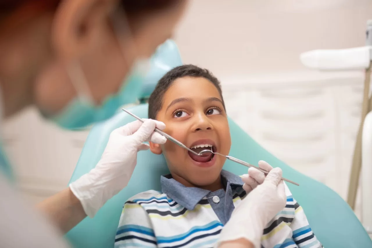 Dentist examining child’s teeth with dental mirror