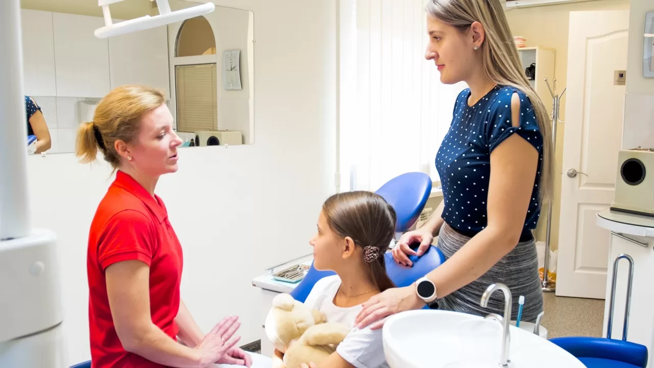 Pediatric dentist speaking with a child and parent in a dental exam room