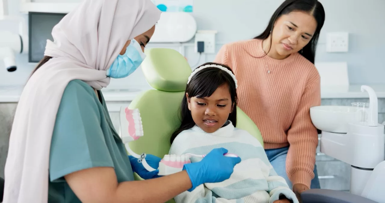 Pediatric dentist teaching a child and parent proper brushing habits