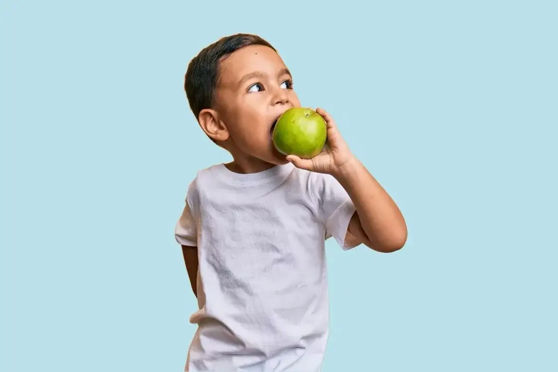 Child eating a green apple against a light blue background